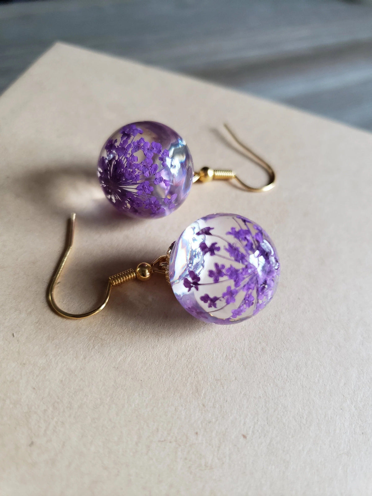 Perle Lilas | Boucles d'oreilles dorées avec fleurs violettes séchées dans une sphère transparente – Vue 01