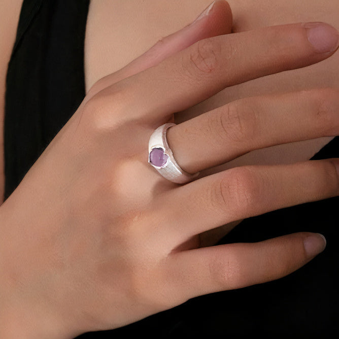Main portant une bague large argentée avec petite pierre rose