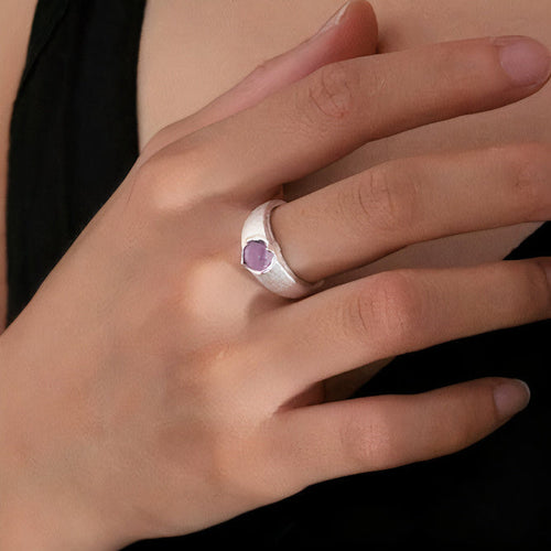 Main portant une bague large argentée avec petite pierre rose