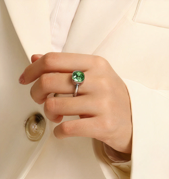 Main portant une bague fine argentée avec pierre verte ronde