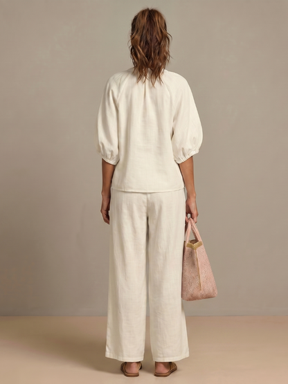 Femme portant un ensemble deux pièces avec blouse zippée et pantalon à jambes larges, coloris blanc