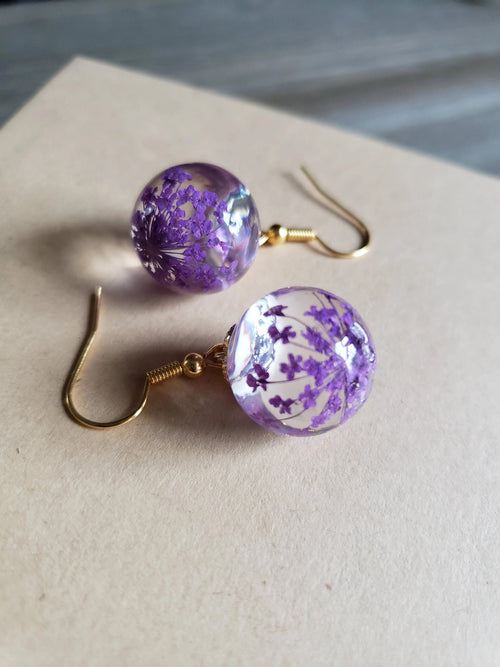 Perle Lilas | Boucles d'oreilles dorées avec fleurs violettes séchées dans une sphère transparente – Vue 01