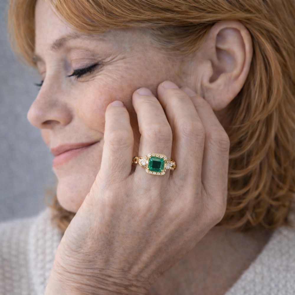 Main portant une bague dorée avec grande pierre verte