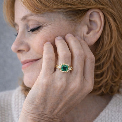 Main portant une bague dorée avec grande pierre verte